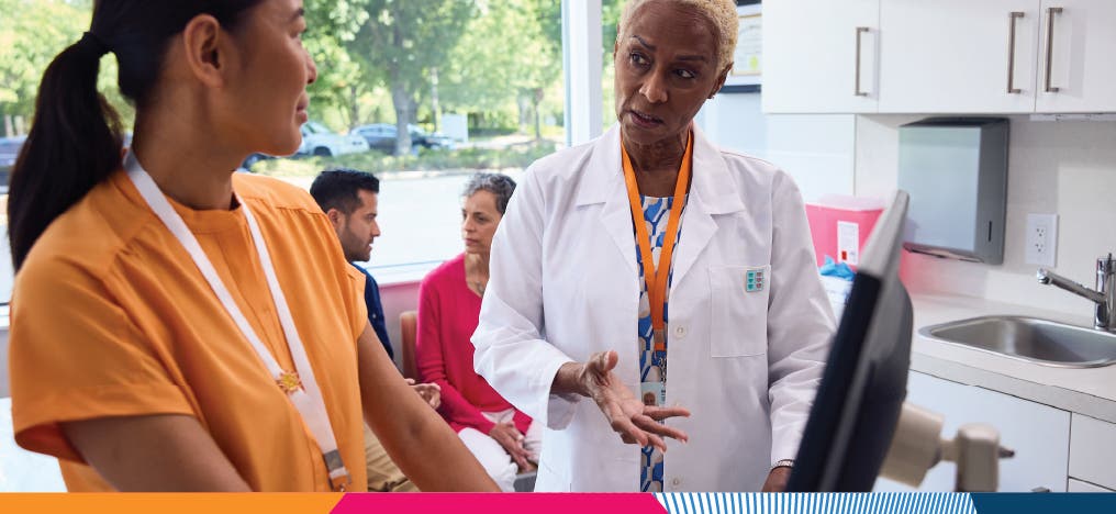 A nurse and a doctor consulting one another in front of a computer in a doctor's front office