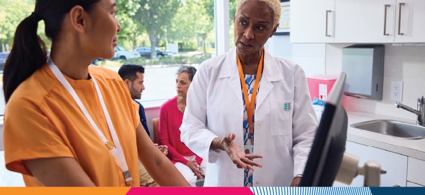 A nurse and a doctor consulting one another in front of a computer in a doctor's front office