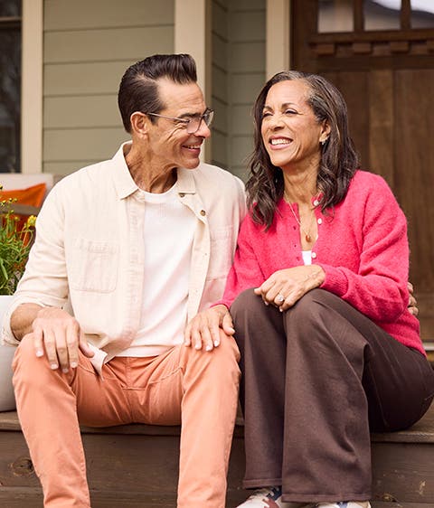 A picture of a middle-aged couple sitting closely together on a porch chatting and laughing.
