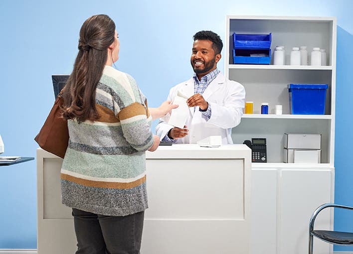A pharmacist handing a patient a prescription across the pharmacy counter