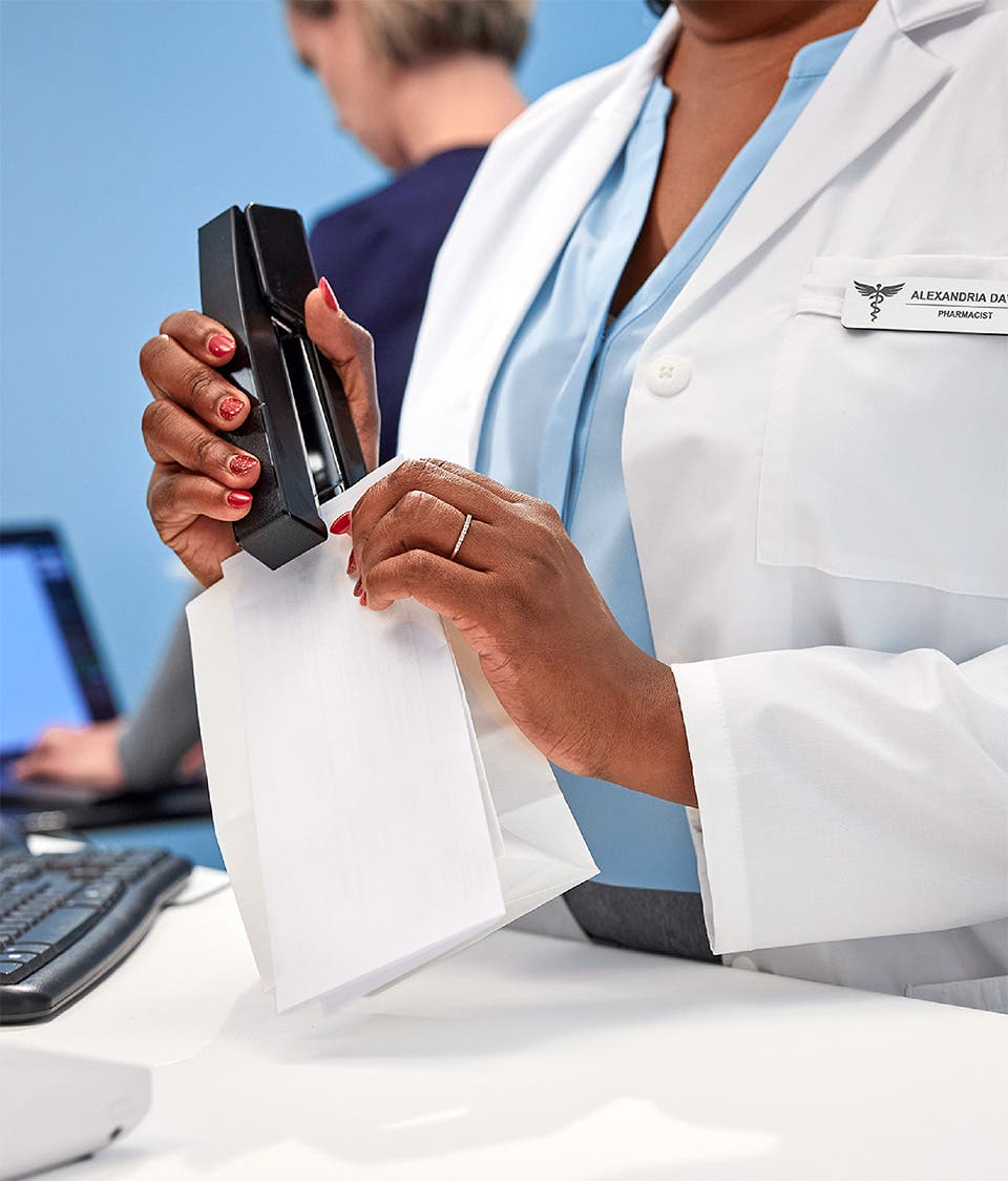 Pharmacist stapling receipt to bag containing prescription medication.