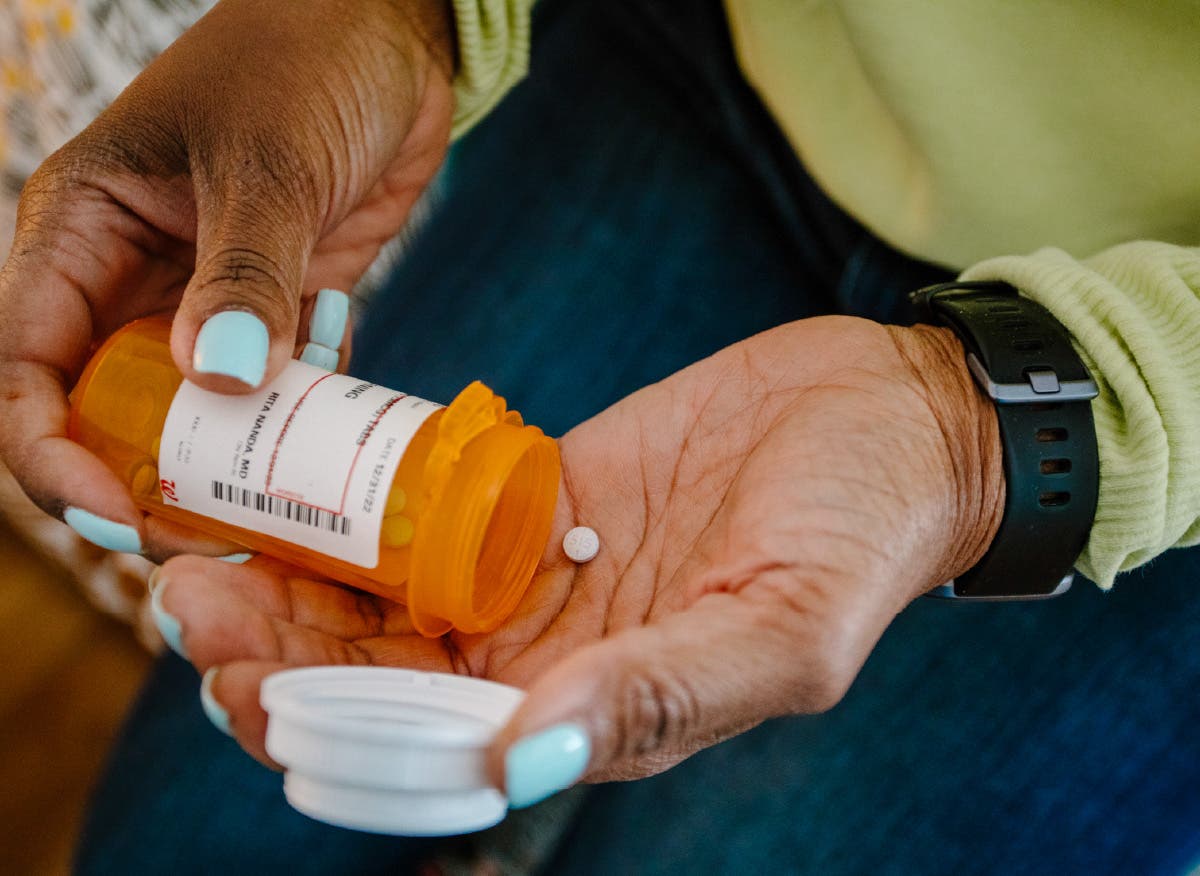 A patient dispensing a single pill from a prescription bottle into her hand.