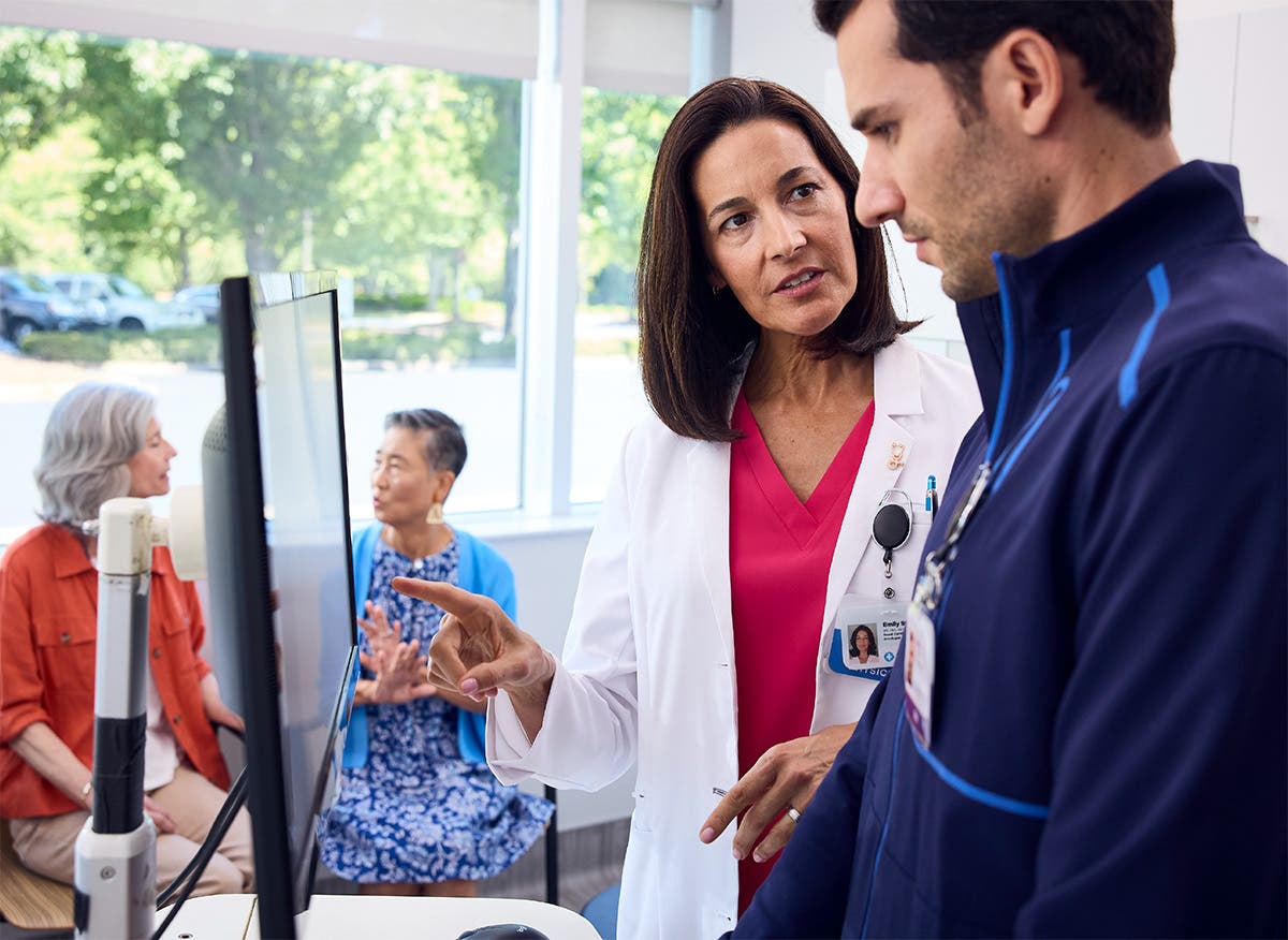 Provider and care team reviewing information on a mobile computer workstation with patient in the background.