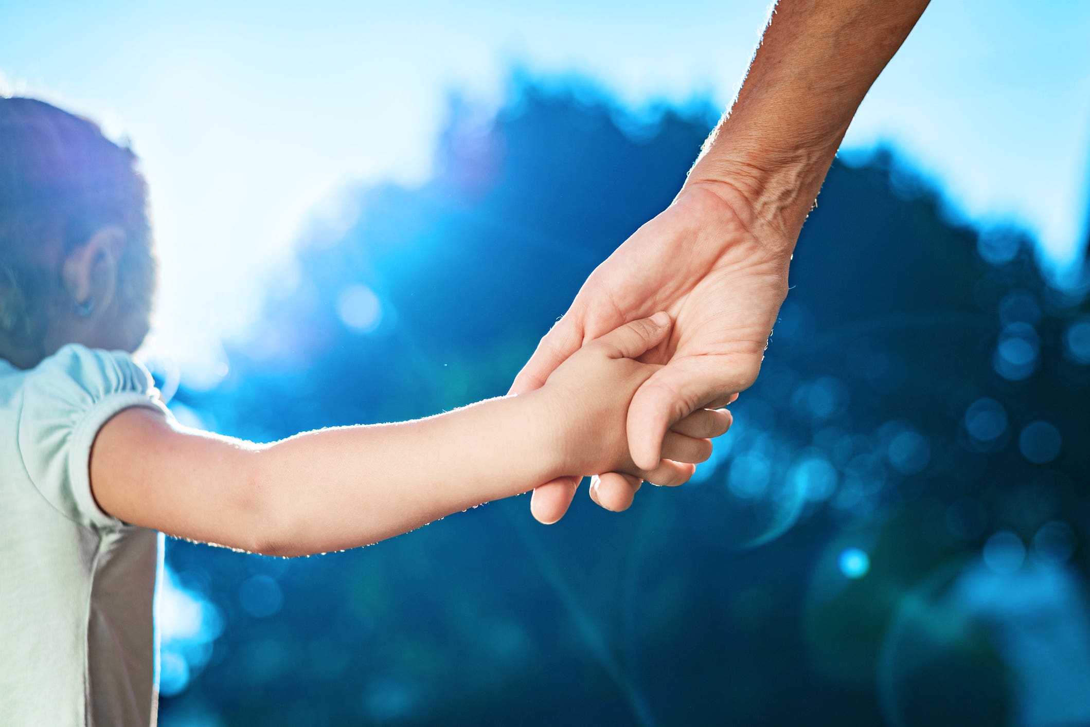 A person holding a child 's hand with a blue sky in the background